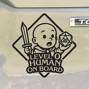 May include: Black and white car decal featuring a baby holding a sword and a 20-sided die. The text reads "LEVEL 0 HUMAN ON BOARD" inside a diamond shape. The decal is on a silver car.