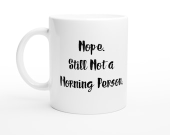 Może przedstawiać: Biały ceramiczny kubek z zakrzywionym uchwytem. Kubek zawiera napis "Nope. Still Not a Morning Person" w czarnym, odręcznym stylu. Kubek jest umieszczony na białym tle.