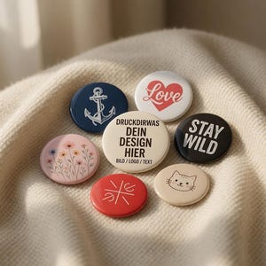 Könnte beinhalten: Sieben runde Ansteckbuttons mit verschiedenen Designs. Die Buttons zeigen einen Anker, das Wort "Love" mit einem Herz, den Text "Stay Wild", ein Blumenmuster, ein Katzenkopf und andere Grafiken und Texte.