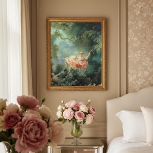 May include: A framed artwork shows a woman on a swing in a verdant forest. The painting has a gold frame and is hung on a beige wall. A bouquet of pink and white roses in a glass vase sits on a mirrored table.