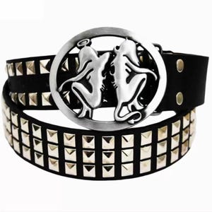 May include: A black belt featuring two rows of silver-toned pyramid studs and a large circular buckle. The buckle displays a silver-toned relief design of two mirrored figures, one with a halo and one with a tail, set within a circular frame.