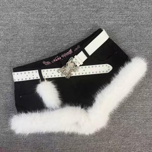 Peut inclure: Short noir avec une bordure en fausse fourrure blanche le long de l'ourlet, associé à une ceinture blanche à clous. La ceinture comprend une boucle papillon argentée et un pompon en fausse fourrure blanche. L'intérieur affiche NaNa Vintage.