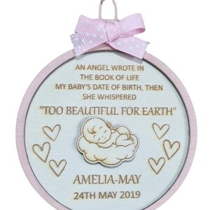 May include: A circular wooden baby keepsake with a pink border and a pink and white polka dot bow. The text reads "AN ANGEL WROTE IN THE BOOK OF LIFE...TOO BEAUTIFUL FOR EARTH." Includes baby's name and birthdate, with heart accents.