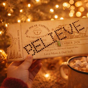 May include: A rectangular wooden ticket for The Polar Express, featuring a train illustration, a bell icon, and the word BELIEVE in black dots. The ticket includes the text Elsie, 25th December 2026, and Love Mum & Dad XXX, with pine tree graphics.