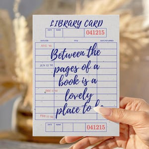 May include: A vintage-style library card with the text "Between the pages of a book is a lovely place to be." The card has a blue and red color scheme, with the number "041215" printed on it.