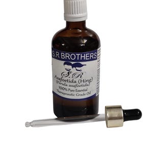 May include: A brown glass bottle of asafoetida oil with a white cap and a dropper. The label reads "S.R BROTHERS Asafoetida (Hing) 100% Pure Essential Therapeutic Grade Oil". The dropper is lying next to the bottle.