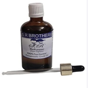 Op de afbeelding: Een bruine glazen fles S.R. BROTHERS Zwarte peper essentiële olie met een witte dop en etiket. Een glazen pipet met een goudkleurige bovenkant en zwarte rubberen bol zit naast de fles. Het etiket luidt "100% Pure Essential Therapeutic Grade Oil."
