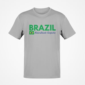 May include: A light gray t-shirt with the word "BRAZIL" in green block letters. Below the word "BRAZIL" is a small Brazilian flag and the words "Naturalmente Campe&otilde;es" in blue script.