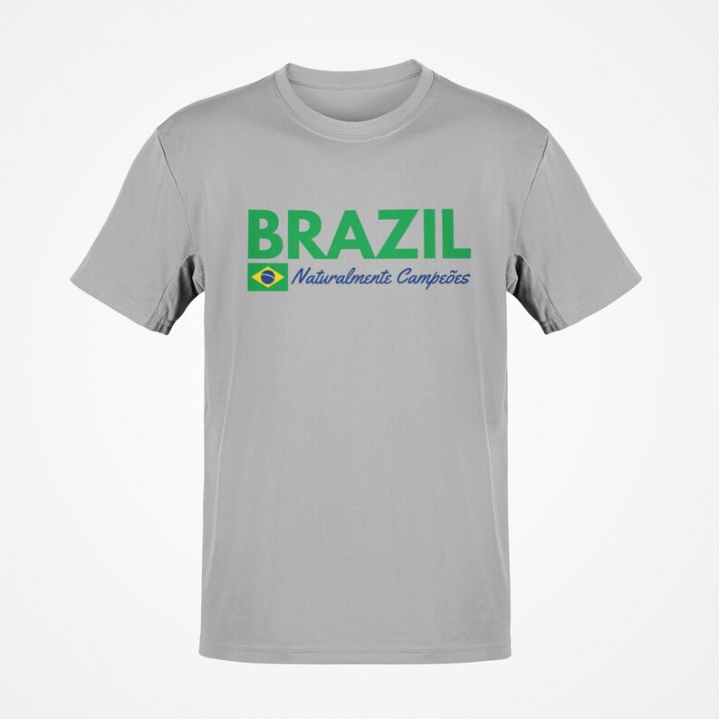 May include: A light gray t-shirt with the word "BRAZIL" in green block letters. Below the word "BRAZIL" is a small Brazilian flag and the words "Naturalmente Campe&otilde;es" in blue script.