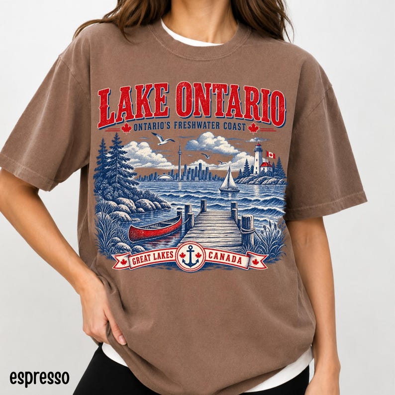 K&ouml;nnte beinhalten: Ein braunes Kurzarm-T-Shirt mit einer Grafik des Lake Ontario. Das Design zeigt ein rotes Kanu, einen Holzsteg, einen Leuchtturm, ein Segelboot und eine Stadtsilhouette. Der Text lautet LAKE ONTARIO, ONTARIO'S FRESHWATER COAST und GREAT LAKES CANADA.