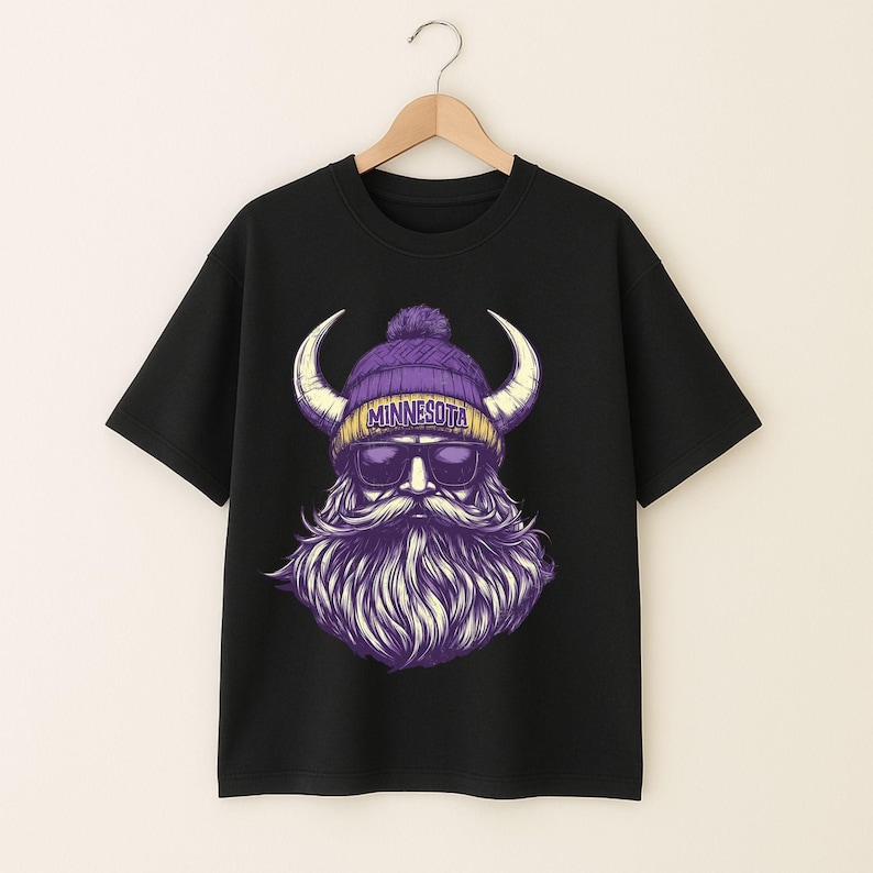 Pu&ograve; includere: T-shirt nera con grafica di un vichingo con berretto viola, occhiali da sole e lunga barba. Sul cappello c'&egrave; la scritta "MINNESOTA". Il vichingo ha grandi corna. La maglietta &egrave; appesa a una gruccia di legno.