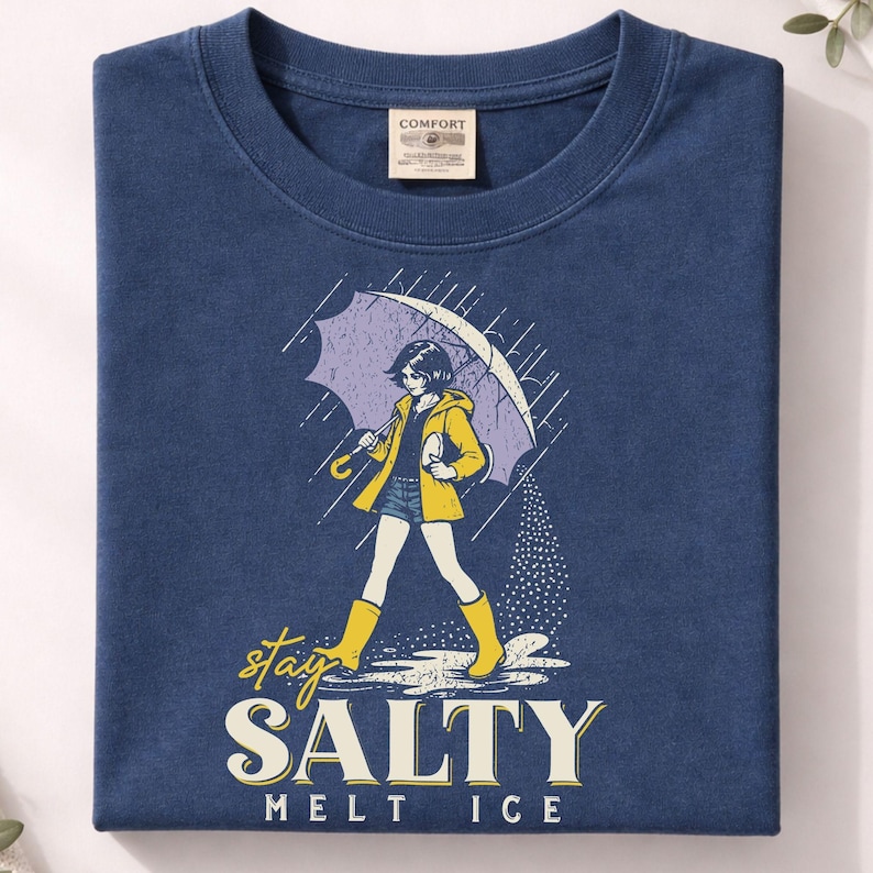May include: Navy blue t-shirt featuring a graphic of a person walking in the rain under an umbrella. The person is wearing a yellow jacket and boots. The text "stay SALTY melt ICE" is below the graphic.