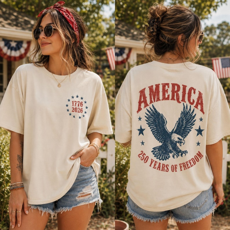 May include: An off-white short-sleeve t-shirt featuring a small circular graphic on the front with blue stars and the text 1776 2026. The back displays a large graphic of a bald eagle, blue stars, and the red text AMERICA 250 YEARS OF FREEDOM.