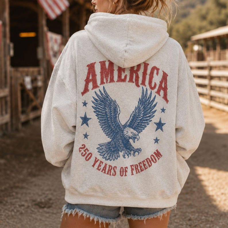 May include: A light gray hoodie with the word "AMERICA" in red, arched across the top. Below is a blue eagle with outstretched wings, surrounded by blue stars. The text "250 YEARS OF FREEDOM" is below the eagle.