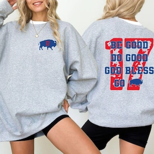 Puede incluir: Una sudadera gris claro con un logotipo de búfalo azul y rojo y el número 17. La parte posterior de la sudadera presenta las palabras "BE GOOD DO GOOD GOD BLESS GO" en rojo y azul.