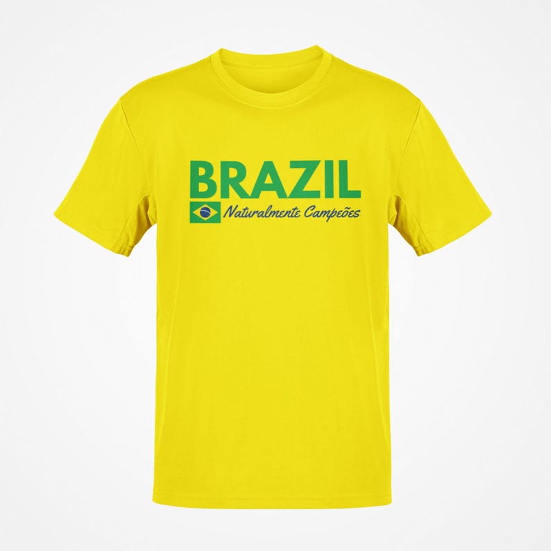 May include: A yellow t-shirt with the word "BRAZIL" in green block letters. Below the word "BRAZIL" is the Brazilian flag and the words "Naturalmente Campe&otilde;es" in green. The shirt has short sleeves and a crew neck.