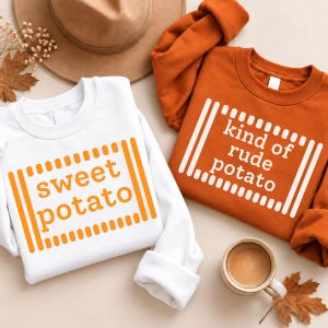 May include: A white sweatshirt with orange text reading sweet potato and an orange sweatshirt with white text reading kind of rude potato. Both feature a barcode-style graphic frame. A brown hat and a ceramic mug are also visible.