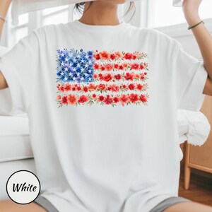 May include: White t-shirt featuring a floral American flag design. The flag's stars are represented by blue flowers, and the stripes are made of red flowers. The word "White" is in a black circle at the bottom left.