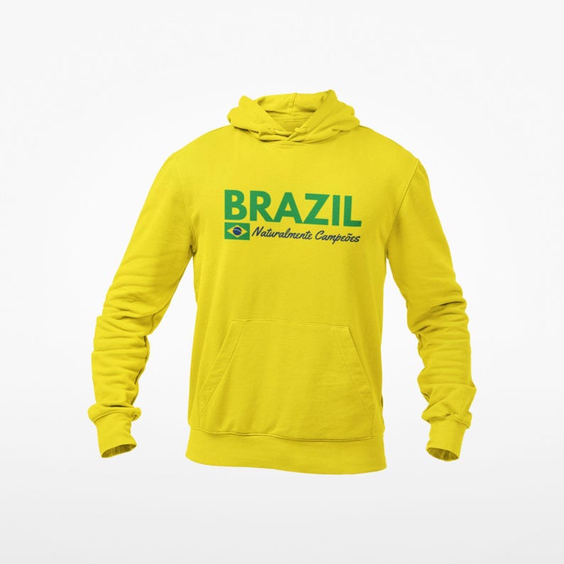 May include: A yellow hooded sweatshirt with the word "BRAZIL" in green block letters. Below the word "BRAZIL" is the Brazilian flag and the words "Naturalmente Campe&otilde;es" in green. The sweatshirt has a front pocket and long sleeves.
