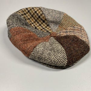Może przedstawiać: Czapka typu newsboy z patchworku w odcieniach brązu, beżu i kremu. Czapka posiada różnorodne, teksturowane tkaniny, w tym wzory w jodełkę i pepitkę. Klasyczny styl, odpowiedni na różne okazje.