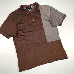 May include: A brown and gray polo shirt with short sleeves. The shirt has a two-tone design, with a brown body and a gray panel on the right side. It features a collar and button closure.