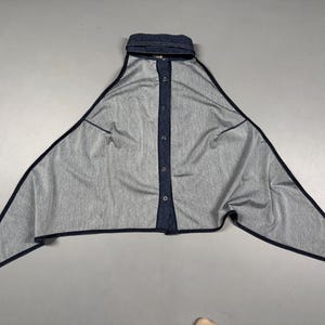 Puede incluir: Top de estilo denim con cuello y cierre de botones. El top tiene un dise&ntilde;o asim&eacute;trico &uacute;nico con bordes largos y puntiagudos y ribete azul oscuro. La tela parece ser un denim de lavado claro.