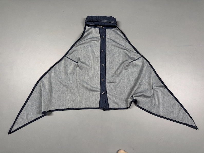 Puede incluir: Top de estilo denim con cuello y cierre de botones. El top tiene un dise&ntilde;o asim&eacute;trico &uacute;nico con bordes largos y puntiagudos y ribete azul oscuro. La tela parece ser un denim de lavado claro.