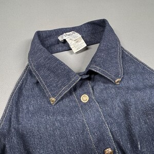 Puede incluir: Una camisa vaquera azul oscuro con cuello cl&aacute;sico y botones dorados. La camisa presenta costuras blancas a lo largo de las costuras y el cuello. La etiqueta dice "Vimsal".