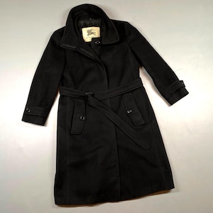 May include: A black wool coat with a belted waist and a notched collar. The coat features long sleeves with buttoned cuffs and a small label near the collar. The coat is a classic style, suitable for various occasions.