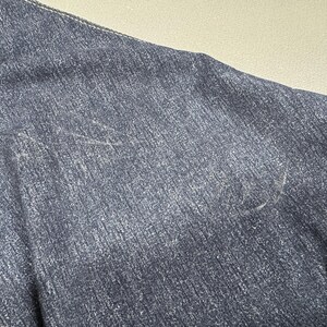 Puede incluir: Primer plano de una chaqueta vaquera azul oscuro. La tela tiene un aspecto texturizado con costuras visibles a lo largo de las costuras. El color de la chaqueta es un &iacute;ndigo profundo, con sutiles variaciones de tono.