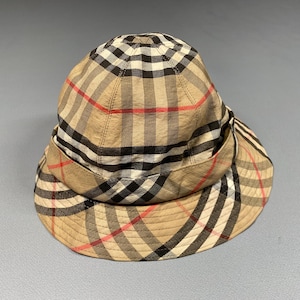 May include: A tan bucket hat with a classic plaid pattern in black, red, and white. The hat features a wide brim and a structured crown. This hat is a stylish accessory for sun protection.
