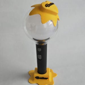 May include: A yellow and black light stick with a clear globe and the word "Butter" on the base. The top of the light stick has a yellow design with the word "Butter" on it. The light stick has a black handle with two buttons.