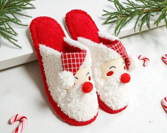 Può includere: Un paio di pantofole festive di Babbo Natale rosse e bianche. Le pantofole hanno una consistenza morbida e soffice con la faccia di Babbo Natale, un naso rosso e un cappello a scacchi. Bastoncini di zucchero e verde sullo sfondo.