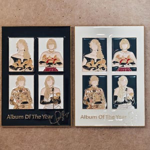 Puede incluir: Dos pines esmaltados rectangulares con cuatro ilustraciones distintas de una persona sosteniendo premios Grammy. El pin izquierdo tiene un borde negro y el derecho uno blanco. Ambos incluyen el texto Album Of The Year y una firma.