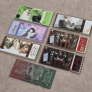 May include: A collection of seven rectangular metal enamel pins shaped like concert tickets. Each pin features unique illustrations and text including Midnights, folklore, Fortnight, Christmas Tree Farm, and Red, showcasing various artistic scenes.