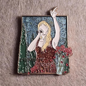 Puede incluir: Pin esmaltado que representa a una cantante rubia con un vestido rojo, sosteniendo un micrófono y señalando hacia arriba. El fondo muestra una escena azul y verde con un jarrón de rosas rojas.