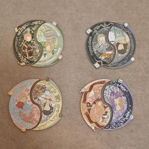 Puede incluir: Cuatro pines circulares de esmalte metálico dispuestos en cuadrícula, cada uno con un diseño de yin-yang dividido en dos escenas ilustradas distintas. Los pines muestran texto que incluye evermore, reputation, Midnights y Red.