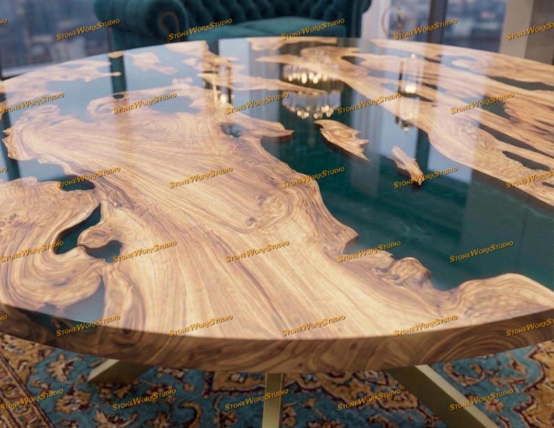 Pu&ograve; includere: Un tavolo rotondo in legno con un design a bordo vivo. Il tavolo presenta un fiume in resina epossidica verde scuro e gambe in metallo color oro. Il legno ha un motivo a venature naturali e il tavolo &egrave; posto su un tappeto fantasia.