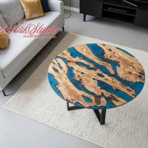 May include: Circular coffee table with a distinctive design. The tabletop combines natural wood and blue resin, forming a flowing pattern. It is supported by a black metal base. The table is approximately 91 cm in diameter.