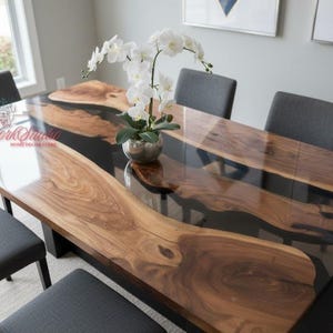 Puede incluir: Mesa de comedor rectangular con diseño de borde vivo. La mesa presenta un centro de resina epoxi transparente y bordes de madera natural. La mesa está rodeada de sillas grises y un jarrón con flores blancas. La mesa mide aproximadamente 183 cm de largo.