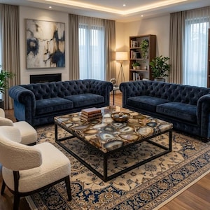 May include: A luxurious living room featuring two navy blue tufted sofas, two white armchairs, and a coffee table with a unique agate stone top. The room includes a patterned rug, a bookshelf, and a large abstract painting.