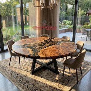 May include: A large, circular wooden dining table with a dark epoxy river design. The table has a black metal base and is surrounded by six upholstered chairs. The table is placed on a patterned rug.