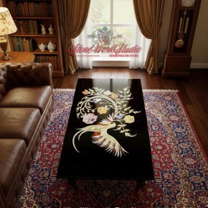 Puede incluir: Una mesa de centro rectangular negra con un diseño de incrustaciones florales y de pájaros. La incrustación presenta elementos blancos, amarillos, rosas y naranjas. La mesa está colocada sobre una alfombra estampada en una habitación con ventana y sofá de cuero.