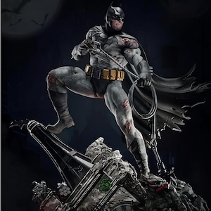Op de afbeelding: Een gedetailleerd standbeeld van Batman, gekleed in een grijs en zwart pak, staat op een gotische structuur. Het figuur houdt een grijphaak en cape vast. Het standbeeld heeft een donkere achtergrond met een volle maan en vleermuizen.