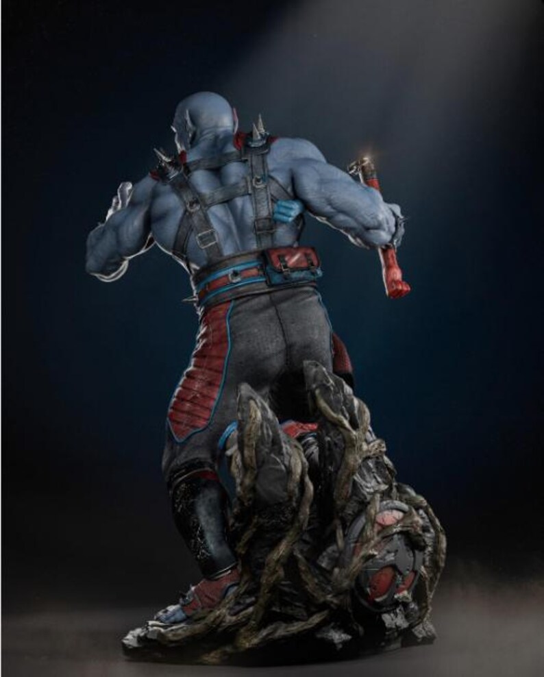 May include: A blue-skinned action figure with a muscular physique, wearing a black and red outfit with a harness and spiked shoulder pads. The figure is holding a red weapon and stands on a detailed, textured base.