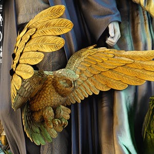 May include: A detailed resin statue of an owl with outstretched wings, featuring gold and green coloration. The owl is part of a larger figure, with a dark blue and gray background. The statue is labeled "Scale 1/6" and "Resin & FDM Portraits".