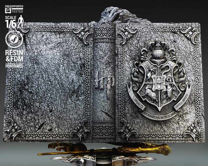 May include: A detailed, gray resin sculpture of an open book with the Hogwarts crest on the right side. The book has intricate detailing and the text "Hp" on the spine. A golden wand rests below the book.