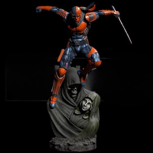 Puede incluir: Figura detallada de un superhéroe en pose dinámica, vestido con armadura naranja y azul, sosteniendo una espada. La figura está sobre una estatua con una figura encapuchada y una calavera. El fondo es negro.