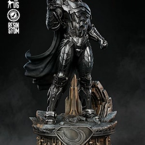 May include: A detailed statue of a character in a dark, metallic suit with a black cape. The figure is standing on a detailed base with a stylized "S" emblem. The statue is pre-supported and made of resin.