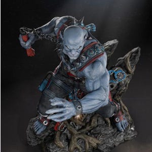 May include: A detailed figurine of a blue-skinned humanoid creature in a dynamic pose. The figure is adorned with spiked shoulder armor, wrist cuffs, and a chain. It is set on a rocky base with intricate details, showcasing a fantasy theme.